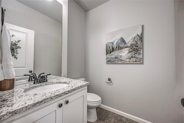 half bathroom with baseboards, vanity, toilet, and wood finished floors