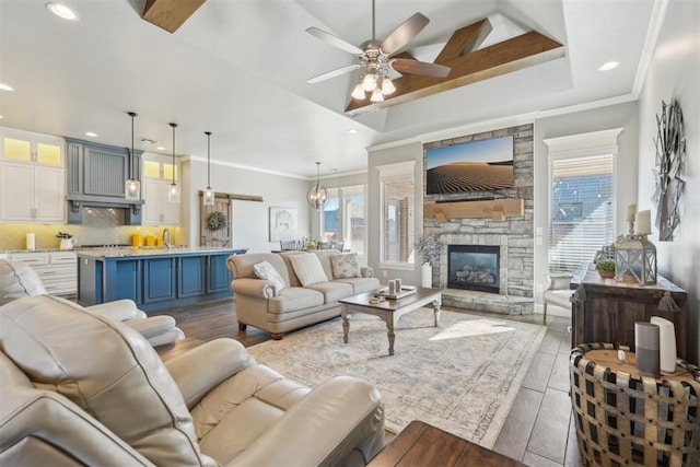 living area with ornamental molding, ceiling fan, a stone fireplace, and light wood-style flooring