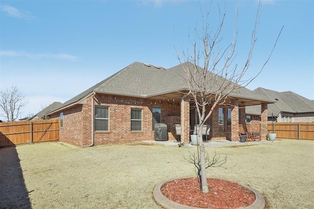 rear view of house featuring a patio, brick siding, a shingled roof, and a fenced backyard