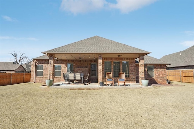 back of property featuring a fenced backyard, roof with shingles, a patio, and brick siding