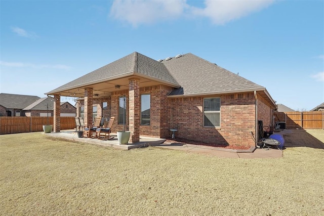 back of property featuring brick siding, a patio, roof with shingles, a lawn, and a fenced backyard