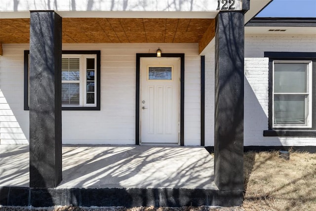 doorway to property with brick siding, a porch, and visible vents