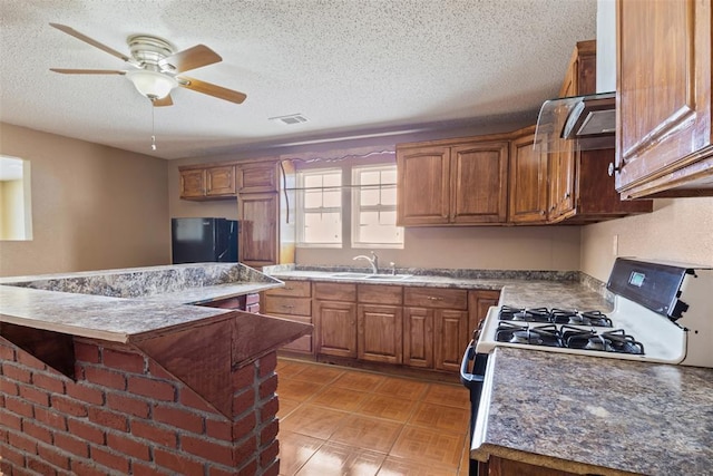 kitchen featuring visible vents, brown cabinetry, gas range, freestanding refrigerator, and a sink