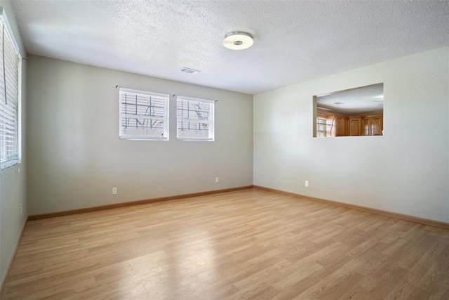 empty room with light wood-type flooring, visible vents, a textured ceiling, and baseboards