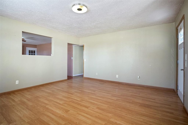 spare room with light wood-style floors, a textured ceiling, and baseboards