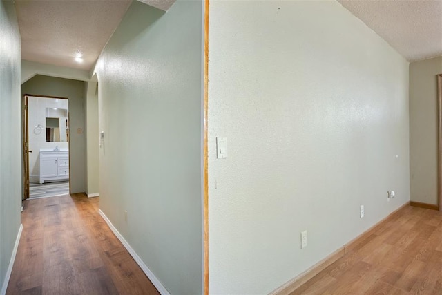 hall featuring baseboards, a textured ceiling, and light wood finished floors