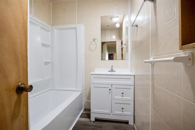 bathroom with wood finished floors, shower / washtub combination, vanity, and tile walls