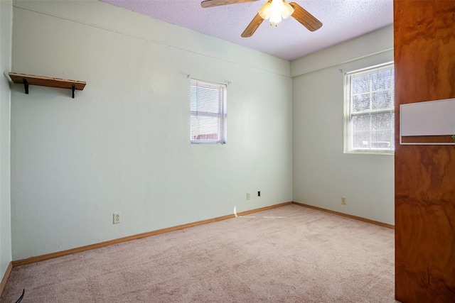 unfurnished room with light carpet, ceiling fan, a textured ceiling, and baseboards