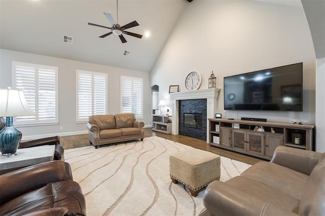 living room featuring high vaulted ceiling, wood finished floors, a glass covered fireplace, and visible vents