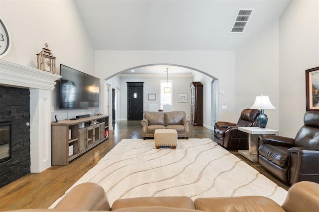 living room featuring arched walkways, crown molding, a fireplace, visible vents, and wood finished floors