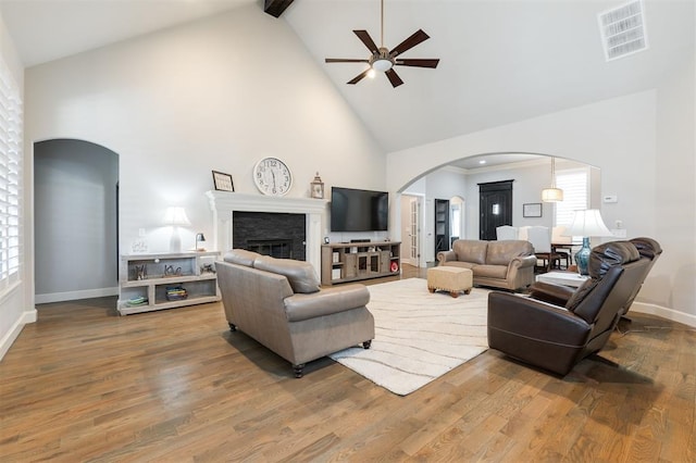 living area with arched walkways, a fireplace, visible vents, wood finished floors, and high vaulted ceiling