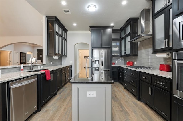 kitchen with arched walkways, visible vents, appliances with stainless steel finishes, light stone countertops, and wall chimney exhaust hood