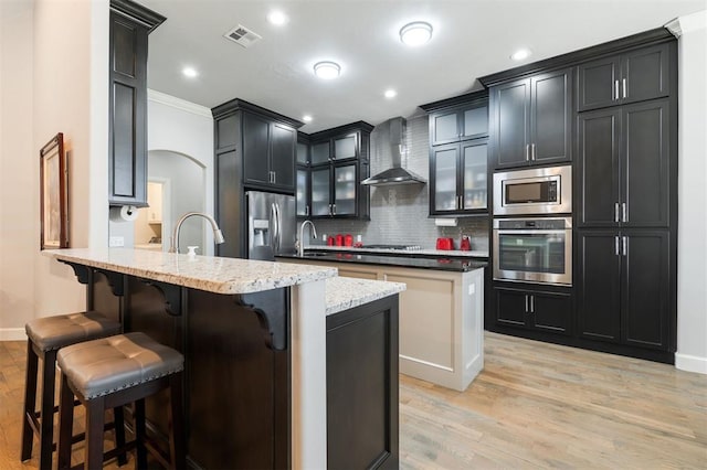 kitchen featuring a peninsula, a kitchen breakfast bar, appliances with stainless steel finishes, wall chimney range hood, and tasteful backsplash