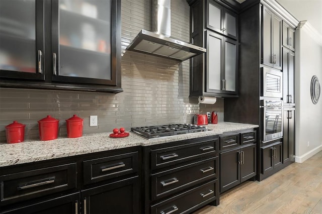 kitchen featuring appliances with stainless steel finishes, light wood-style floors, decorative backsplash, and wall chimney exhaust hood