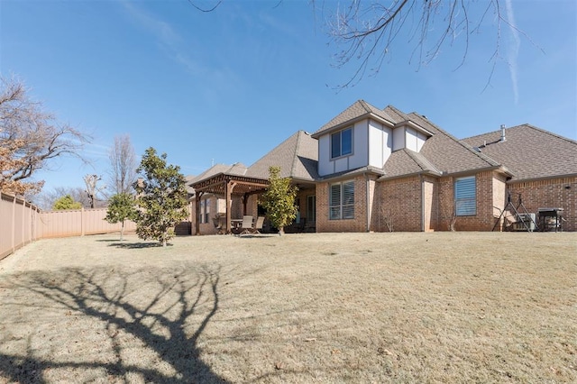 rear view of house featuring a yard, brick siding, roof with shingles, and a fenced backyard