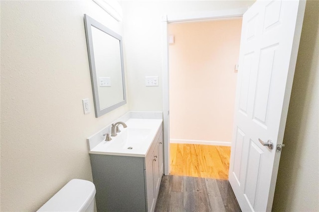 half bath featuring toilet, baseboards, wood finished floors, and vanity