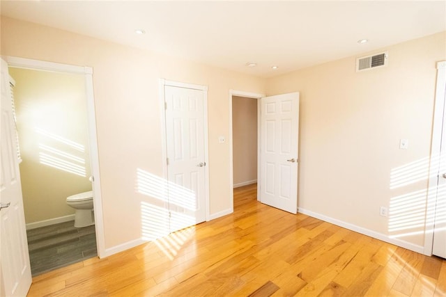 unfurnished bedroom with ensuite bathroom, light wood finished floors, visible vents, and baseboards