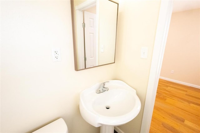 half bathroom with baseboards, a sink, toilet, and wood finished floors