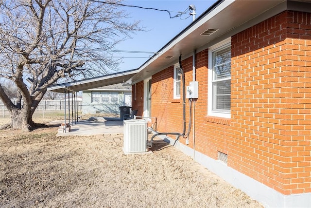 view of property exterior with a patio, cooling unit, brick siding, fence, and crawl space