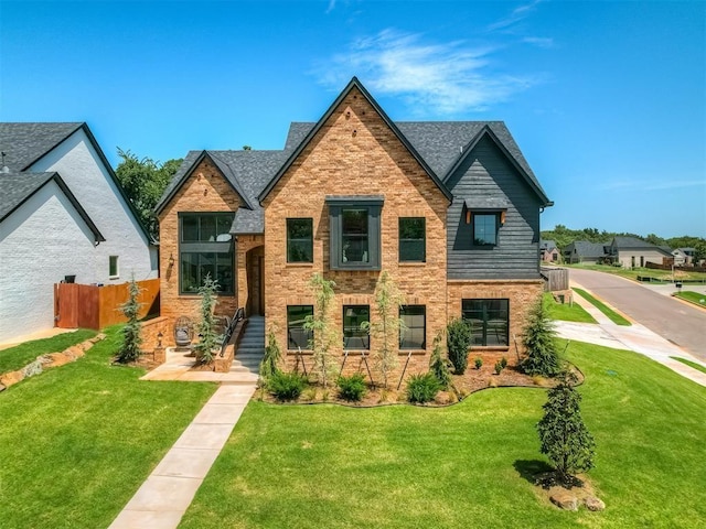 view of front facade featuring a shingled roof, fence, a front lawn, and brick siding