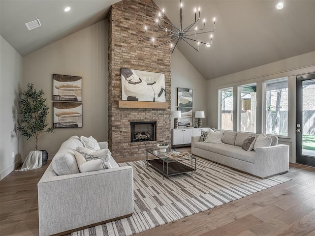 living area featuring high vaulted ceiling, a fireplace, wood finished floors, and an inviting chandelier