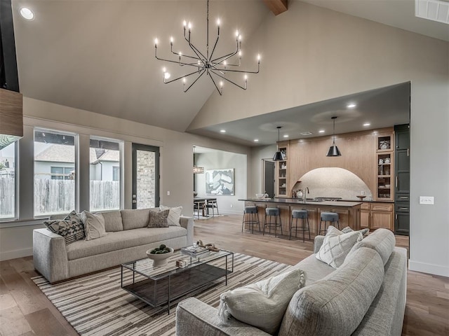 living area featuring light wood finished floors, a chandelier, visible vents, high vaulted ceiling, and baseboards