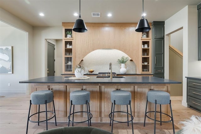 kitchen with dark countertops, visible vents, decorative backsplash, light wood-style floors, and a sink