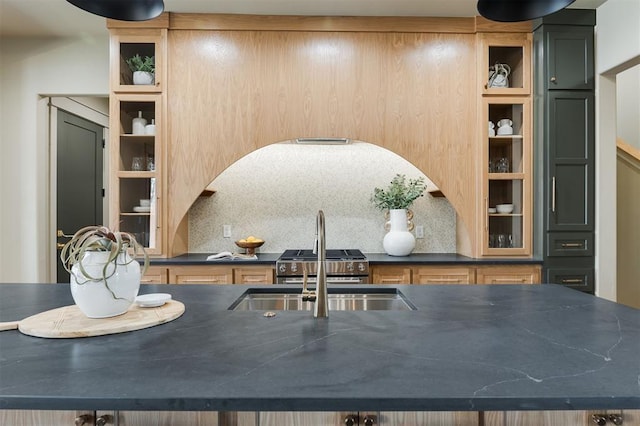 kitchen featuring a sink, dark countertops, backsplash, and glass insert cabinets