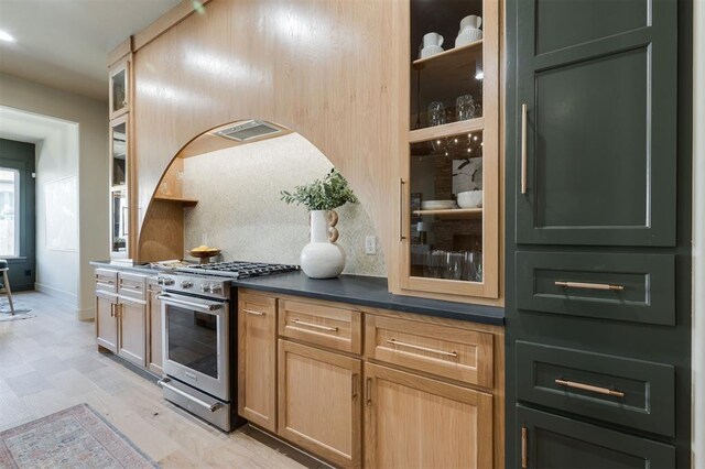 kitchen with stainless steel gas range, dark countertops, glass insert cabinets, and decorative backsplash