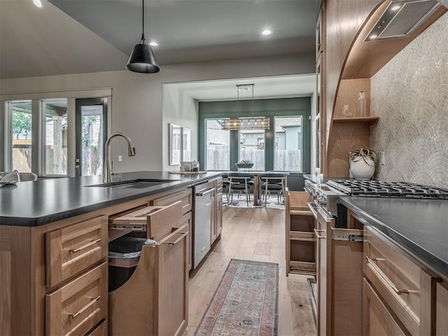 kitchen with stainless steel appliances, dark countertops, brown cabinetry, a sink, and light wood-type flooring