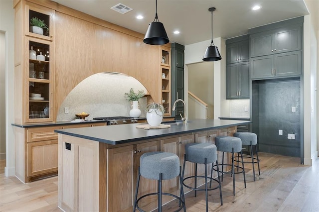 kitchen with light wood-type flooring, visible vents, a sink, and an island with sink