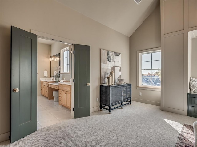 bedroom featuring multiple windows, high vaulted ceiling, connected bathroom, and light colored carpet