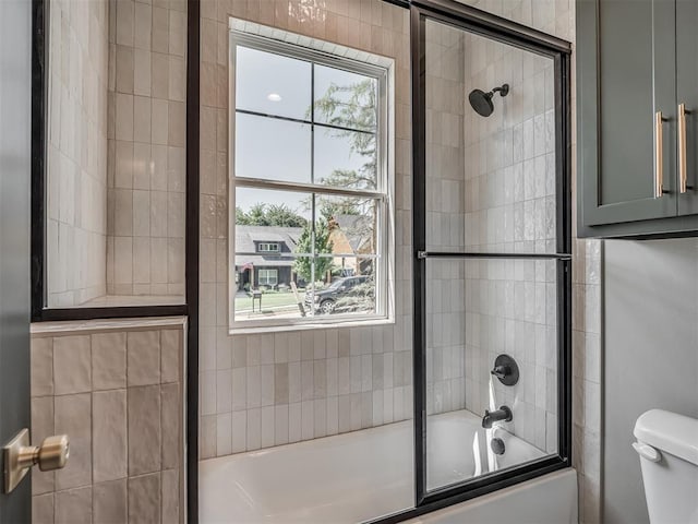 bathroom featuring toilet and bath / shower combo with glass door