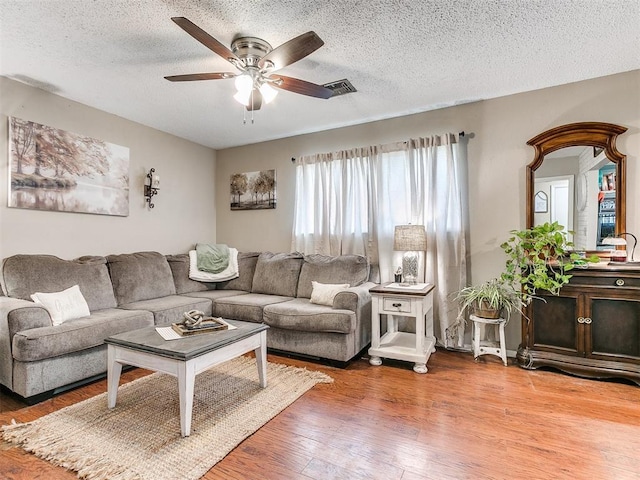 living area with light wood-style floors, a textured ceiling, visible vents, and a ceiling fan