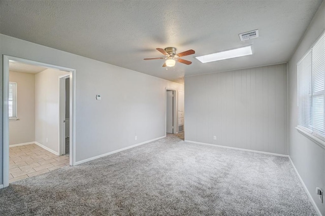 carpeted empty room with a skylight, a ceiling fan, visible vents, and a textured ceiling