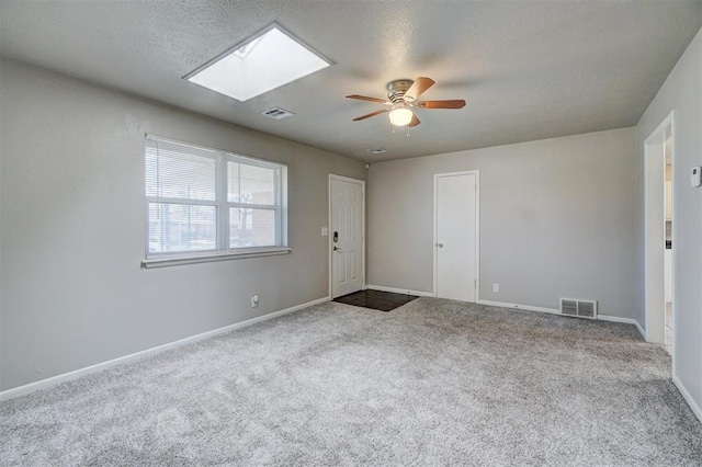 empty room with carpet floors, a skylight, visible vents, and baseboards