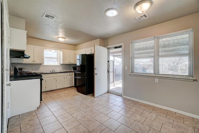 kitchen with under cabinet range hood, visible vents, stainless steel range with gas cooktop, freestanding refrigerator, and dark countertops