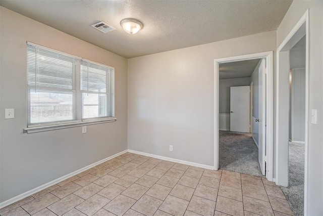 unfurnished room featuring light tile patterned floors, a textured ceiling, visible vents, and baseboards