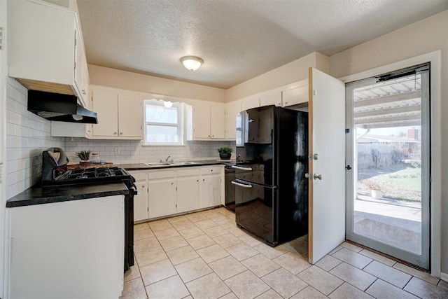 kitchen featuring range with gas stovetop, dark countertops, freestanding refrigerator, a sink, and under cabinet range hood