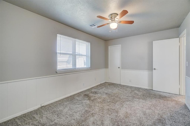 unfurnished room with carpet floors, wainscoting, visible vents, and a textured ceiling