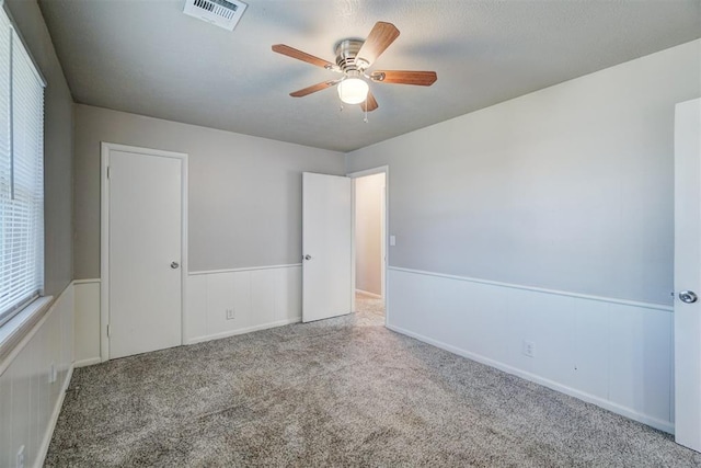 empty room with carpet, visible vents, ceiling fan, and wainscoting