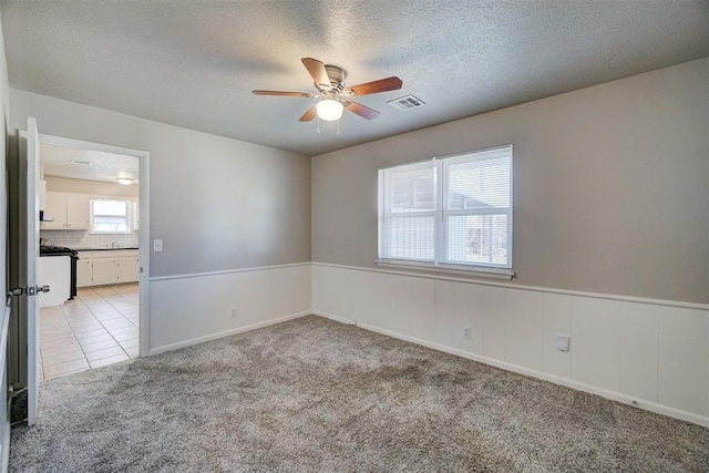 empty room with light carpet, visible vents, a wainscoted wall, a textured ceiling, and light tile patterned flooring