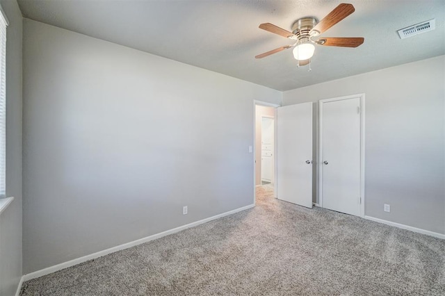 carpeted empty room featuring baseboards, visible vents, and ceiling fan