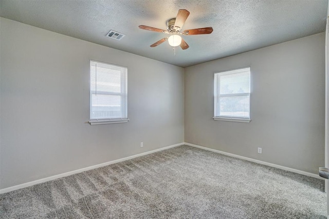 carpeted spare room featuring a healthy amount of sunlight, baseboards, visible vents, and a textured ceiling