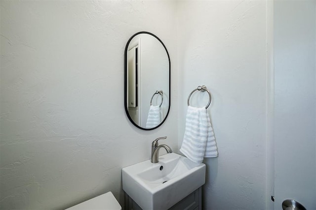 bathroom with toilet, a textured wall, and vanity