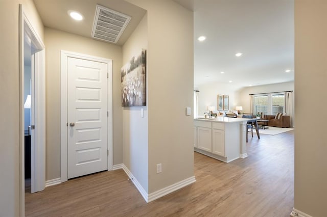 hallway with light wood finished floors, recessed lighting, visible vents, a sink, and baseboards