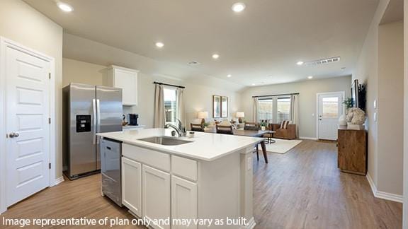 kitchen with light wood finished floors, appliances with stainless steel finishes, open floor plan, white cabinets, and a sink