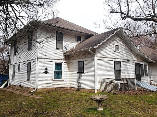 rear view of house with entry steps, a lawn, and roof with shingles