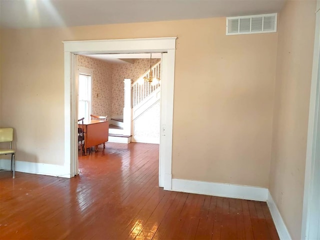 unfurnished room featuring wallpapered walls, wood-type flooring, visible vents, and baseboards