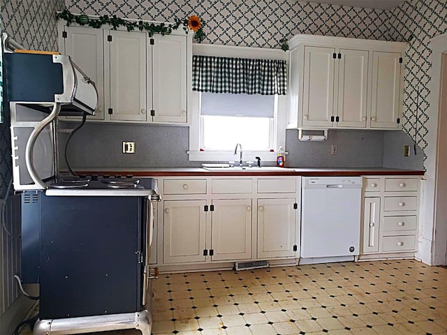 kitchen with wallpapered walls, dishwasher, light floors, white cabinetry, and a sink